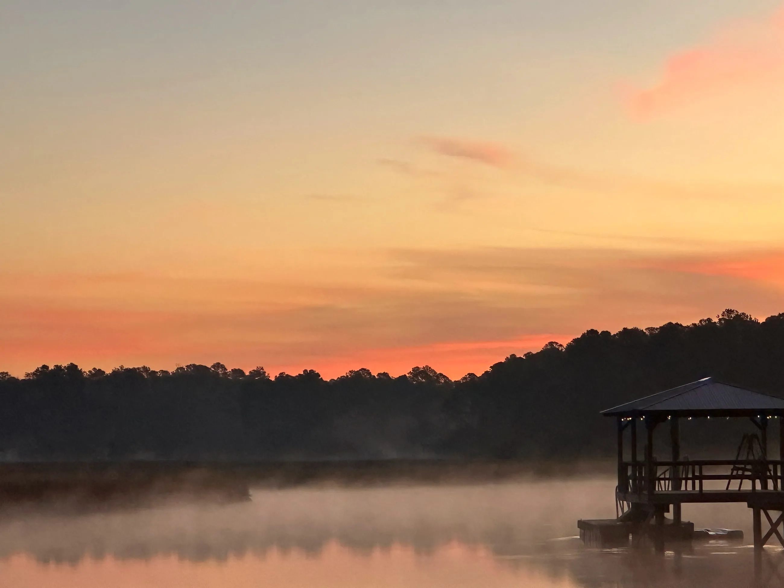 Sunrise over a coastal Georgia tidal marsh, with a dock silhouetted against a coral sky and mist sitting on the water.